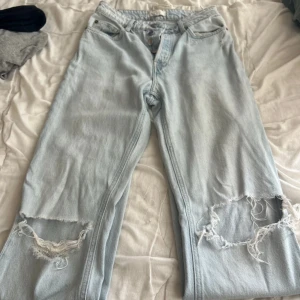 Ljusblå ripped jeans från H&M - Säljer ett par ljusblå jeans från H&M med snygga slitningar och hål vid knäna. Modellen är rak med låg midja och klassiska fem fickor. Perfekta för en avslappnad och trendig look.