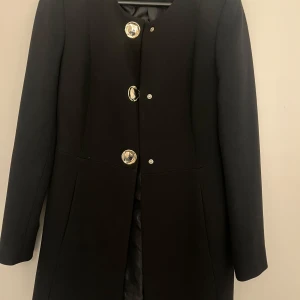 Svart kappa från Zara med stora knappar Storlek S - Säljer en svart kappa från Zara med stora, dekorativa silverfärgade knappar framtill. Kappan har rund halsringning, långärmad och klassisk rak passform, passar både höst och vår. 