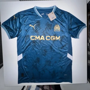 Puma x Marseille fotbollströja  - Snygg marinblå Olympique de Marseille fotbollströja från Puma. STORLEK M!  guldfärgade detaljer och klubbmärke på bröstet. Tröjan har korta ärmar, vit kant vid kragen och är tillverkad i ett lätt funktionsmaterial. Perfekt för dig som älskar fransk fotboll.
