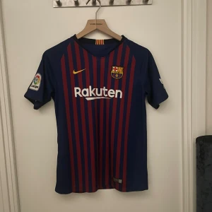 FC Barcelona Messi #10 matchtröja - Säljer en äkta officiell FC Barcelona fotbollströja från Nike med Messi #10 på ryggen. Tröjan är blå med röda vertikala ränder, har La Liga-märke på ärmen och Rakuten som sponsor på bröstet. Klassisk rund hals och korta ärmar, tillverkad i lätt och ventilerande material. Ny pris 1600 