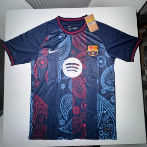 Barca X Nike fotbollströja  - Snygg FC Barcelona fotbollströja från Nike i mörkblått med paisleyinspirerat mönster i rött och ljusblått. STORLEK S! Tröjan har klubbmärke, Nike-logga och Spotify-sponsor på bröstet. Tillverkad i lätt funktionsmaterial och har korta ärmar.