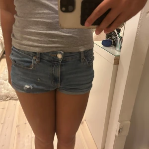 Blå jeansshorts från Gina Tricot - Snygga blå jeansshorts från Gina Tricot med låg midja och slitna detaljer framtill. Shortsen är i storlek 146 men passar större storlekar eftersom dom är väldigt stretchiga.