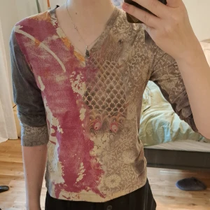 Mönstrad v-ringad tröja Kello - Unik långärmad tröja från Kello med v-ringning. Tröjans mönster består av flera färger i beige, grått och rosa/rött. Materialet är mjukt och stretchigt. Om ni vill se fler bilder eller har en fråga är det bara att höra av sig <3