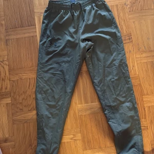 Gröna träningsbyxor från Under Armour - Snygga gröna träningsbyxor från Under Armour med elastisk midja och dragsko. Byxorna har raka ben, sidofickor och en bakficka. Lätta och luftiga i syntetmaterial, perfekta för träning eller chill. Använder inte längre. Vill få bort den så snabbt som möjligt!!!