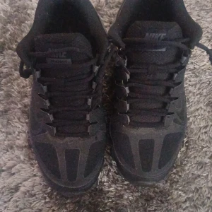 Svarta Nike Training sneakers - Svarta Nike Training sneakers med cool design och robust sula. Skorna har snörning och meshdetaljer för extra andningsförmåga. Swoosh-logga på sidan och diskret Nike-märke på plösen. Perfekta för dig som gillar sportig och stilren look.