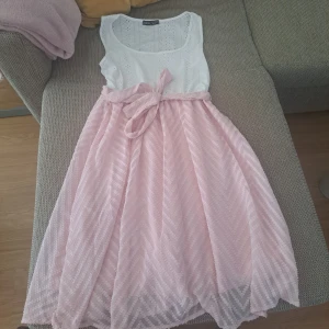 Söt rosa och vit sommarklänning med rosett - Superfin ärmlös klänning från New Look med vit broderad överdel och ljusrosa kjol i transparent tyg med subtilt mönster. Midjan markeras av ett matchande knytband. Perfekt för varma dagar och studentfirande!