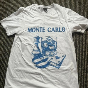 Vit t-shirt med blått Monte Carlo-tryck - Helt ny och oanvänd! Riktigt fet t-shirt, kan sänka priset vid snabb affär!🙌 Snygg vit t-shirt med blått tryck framtill där det står 'Monte Carlo' och motiv av schackpjäs, drinkglas och spelkort. Klassisk passform och rund halsringning. Perfekt för dig som gillar unika prints och chill vibe.