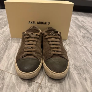 Axel Arigato Cap-Toe sneakers militärgrön - Snygga sneakers från Axel Arigato i militärgrön mocka med cap-toe i mörkare ton. Klassisk låg modell med snörning och vit sula. Perfekta för dig som gillar stilrena och trendiga skor med en twist.
