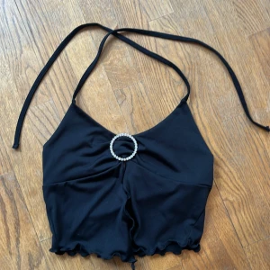 Svart halterneck topp med strassring - Svart croppad halterneck topp med  strassring framtill som detalj. Strl 36! Toppen har volangkant nertill och knytband i nacken. 