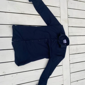 Mörkblå skjorta från Bläck XS - Snygg mörkblå skjorta från Bläck i slim fit-modell. Skjortan har klassisk krage, långa ärmar och knäppning framtill. Perfekt för dig som gillar en stilren och enkel look. Storlek XS (35/36). Köpt ifrån mq marqet och använt endast ett fåtal gånger då den blivit för liten. Nypris runt 1200kr. Priset är ej hugget i sten.