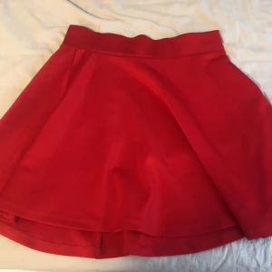 Röd kortkjol med utsvängd passform - Snygg röd kortkjol med bred linning och lätt utsvängd modell. Kjolen är enfärgad och har en enkel, stilren look som är lätt att matcha. Perfekt för dig som vill ha en poppig färg i garderoben!