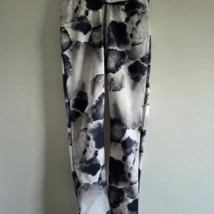 Hyperfied mönstrade träningsbyxor - Snygga träningsbyxor från Hyperfied med svart och grått abstrakt mönster på vit botten. Byxorna är tillverkade i stretchigt material (81% polyester, 19% elastan) och har en bekväm passform med resår i midjan. Perfekta för träning eller chill. En liten fläck på ett ställe, se sista bilden. 