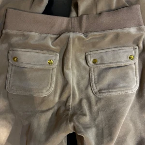Beige mjukisbyxor med guldiga detaljer ( juicy couture ) - Snygga beige mjukisbyxor i mjukt material med bred resår och snörning i midjan från juicy couture 💓. Byxorna har stora fickor bak med guldiga knappar och coola detaljer framtill, perfekt nu till hösten !  En fläck framtill som absolut syns mycket mer på kameran än vad den gör i verklighet  😌  nypris 1200kr, och säljs nu för 550 efftersom fläcken skull. Annars inget fel på byxorna, super fina 🤞🏽 bara skriva om ni har funderingar!! ( har även tröjan till, som jag säljer för 400kr bara för bilder) 💓