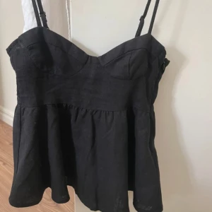 Svart linnetopp från H&M Divided - Supersöt svart linnetopp från H&M Divided med justerbara tunna axelband och markerad byst. Toppen har en lätt utställd, flowy passform nedtill och är tillverkad i en skön linneblandning. Perfekt för varma dagar och enkel att styla med jeans eller kjol.