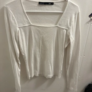 Vit ribbad långärmad topp Lager 157 - Säljer en vit långärmad topp från Lager 157 med fyrkantig halsringning och ribbad struktur. Modellen är slim och sitter snyggt mot kroppen. Perfekt att styla med jeans eller kjol för en clean look.