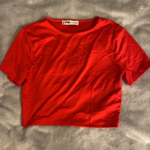 Röd croppad topp från Sister - Snygg röd croppad topp från Sister i mjukt och stretchigt material. Enkel design med rund halsringning och korta ärmar, perfekt för att matcha med höga jeans eller kjol. Färgen är riktigt klar och poppar verkligen. Passar dig som gillar att sticka ut.
