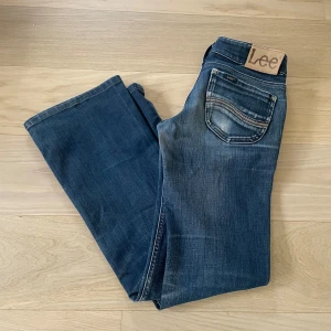 Mörkblå bootcut jeans från Lee - Snygga mörkblå jeans från Lee med klassisk bootcut passform och låg midja. Lee-logga på bakfickan. Tillverkade i mjukt denim-material som sitter skönt och ger en cool siluett. W25 L31