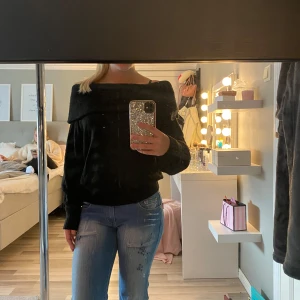 Svart offshoulder stickad tröja - Säljer en svart stickad tröja med offshoulder-design. Tröjan har en bred krage som går över axlarna och långa ärmar. Perfekt till hösten eller vintern.