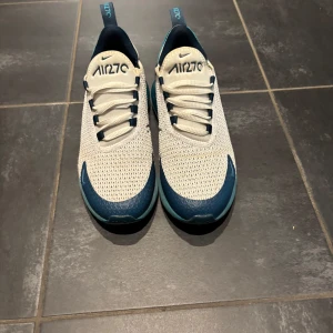 Nike Air 270 sneakers blå/vit - Nike Air 270 sneakers i fräsch vit mesh med blå detaljer och turkosblå sula. Skorna har snörning, rund tå och synlig air-bubbla i hälen. Perfekta för dig som gillar sportig och modern stil. Snygg kontrast mellan färgerna och riktigt bekväma på foten.