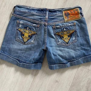 Blå jeansshorts från Take Two - asfina vintage lågmidjade jeansshorts från Take Two som jag köpte second hand i Amsterdam. W27. Midjemått ca 36, dragkedjan är ca 7 cm. Säljer då de tyvärr inte passar mig. De har broderi på de bakre fikorna och har dekorativa nitar framtill. Märkespatch i bak som tyvärr är lite sliten och har några lösa trådar. Fickorna i bak är tyvärr också lite slitna, men det påverkar inte funktionen. Går att vika en extra gång ifall man inte gillar längden. Stretchar knappt. Går att komma med prisförslag. 