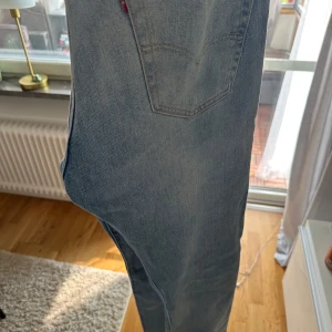 Levi's 501 ljusblå jeans W32 L32 - Klassiska Levi's 501 jeans i ljusblå tvätt med raka ben och knappgylf. Jeansen har fem fickor och den ikoniska läderpatchen bak i midjan. Perfekta för en avslappnad och tidlös stil. Tillverkade i slitstarkt bomullsjeans.