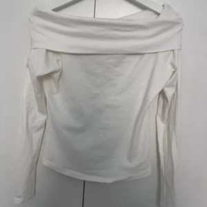 Vit offshoulder långärmad topp - Snygg vit offshoulder topp med långa ärmar och bred krage som vilar över axlarna. Enkel och stilren design som passar perfekt till jeans eller kjol. Mjuk och skön känsla, perfekt för dig som gillar minimalistisk stil. Endast använd 1 gång