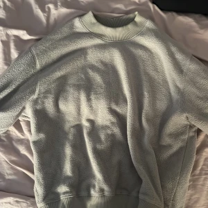 Ljusgrön fleece-tröja från Weekday - Mjuk och chill ljusgrön fleece-tröja från Weekday i storlek M. Tröjan har ribbade muddar vid hals, ärmslut och nederkant, och är perfekt för kalla dagar. Enkel och clean design utan mönster eller detaljer, med lång ärm och loose passform.