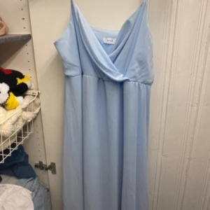 Ljusblå långklänning från Vila Balklänning  - Säljer en ljusblå långklänning från Vila med omlott-detalj vid halsen. Klänningen är ärmlös och har en mjuk, flowy passform som ger en chill vibe. Materialet är skönt och lätt polyester, perfekt för varma dagar. Enkel och stilren design som känns fräsch och modern.