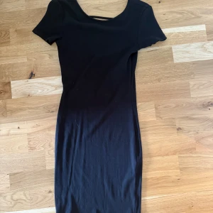 Svart ribbad kortklänning med öppen rygg - Säljer en svart ribbad kortklänning med  korta ärmar. Baksidan har en snygg djup öppen rygg med en tunn rem upptill. 