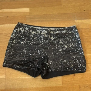 Svarta paljettshorts från Amisu - Glittriga svarta shorts från Amisu, täckta med silvriga paljetter som ger en riktigt festlig vibe. Modellen är kort och har en slim passform med elastisk midja. Perfekta för att sticka ut och glänsa på nästa event. Materialet är mjukt på insidan och paljetterna täcker hela ytan.  Den är lite sliten på sidan men inget som är sönder helt igenom.