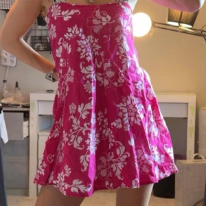 Rosa blommig klänning - Säljer en superfin rosa kortklänning med vita blommor. Klänningen har en luftig passform och är ärmlös. Den har dragkedja baktill. Storlek M. Kan även användas som kjol om man vil.