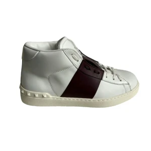 Valentino Garavani vita sneakers - Snygga vita sneakers från Valentino Garavani med vinröd detalj på sidan och klassiska nitar på sulan. Skorna har snörning och är tillverkade i skinn för en lyxig känsla. Perfekta för dig som vill sticka ut med stilrena detaljer.