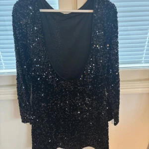 Svart glittrig paljettklänning H&M - Säljer en svart kort paljettklänning från H&M i storlek M. Klänningen har långärmade ärmar och en djup öppen rygg som ger en snygg och festlig vibe. Hela klänningen är täckt av glittriga paljetter som verkligen sticker ut. Perfekt för dig som vill glänsa på nästa event!