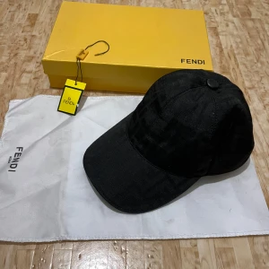 Svart keps från Fendi i bomull - Exklusiv svart keps från Fendi med diskret FF-mönster i tyget. Kepsen är tillverkad i 100% bomull och har justerbar rem baktill med Fendi-logga i läder. Snygg och stilren accessoar som lyfter din outfit. Pris kan diskuteras 