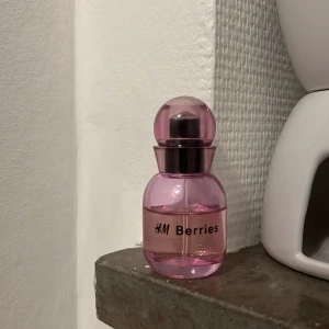 H&M Berries parfym rosa flaska - Söt parfym från H&M med namnet Berries. Kommer i en rund, rosa plastflaska med kupolformat lock och svart spraydel. Flaskan är genomskinlig och har en modern, lekfull design som sticker ut i badrumshyllan.