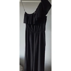 Svart oneshoulder byxdress H&M - Svart byxdress från H&M med oneshoulder och volangdetalj upptill. Jumpsuiten har resår i midjan för en snygg passform och är perfekt för dig som gillar stilrena och trendiga plagg. Materialet känns lätt och flowy. Croppad längd på byxbenen. Använd vid formella tillställningar och sparsamt använd 🌟 pris kan diskuteras 