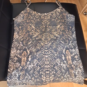 Zara linne med ormmönster - Säljer ett linne från Zara med smala axelband och coolt ormmönster i svart, beige och grått. Perfekt för dig som gillar djurmönstrat och vill sticka ut lite extra. Snygg passform och lätt material som känns skönt mot huden. Oanvänt.