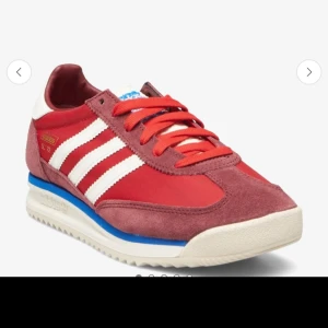 Adidas SL 72 röda sneakers - Adidas SL 72 sneakers i rött med klassiska vita ränder och blå detalj på sulan. Ovandel i textil och mocka, vita snedställda stripes och guldlogga på sidan. Snygg retrostil med röd innersula med Adidas-tryck. Perfekta för dig som gillar old school vibes.