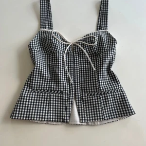 Populär korsettopp - Supersnygg svartvit rutig korsettopp från Zara med breda axelband och söt snörning framtill. Toppen har en figurnära passform och är tillverkad i bomullsmaterial. Perfekt att styla med jeans eller kjol för en trendig look.
