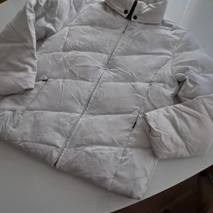 Vit dunjackan från Mexx - Säljer en stilren vit dunjackan från Mexx. Jackan har en dragkedja framtill och är tillverkad i polyester och viskos. Perfekt för kyligare dagar med sin vadderade design.