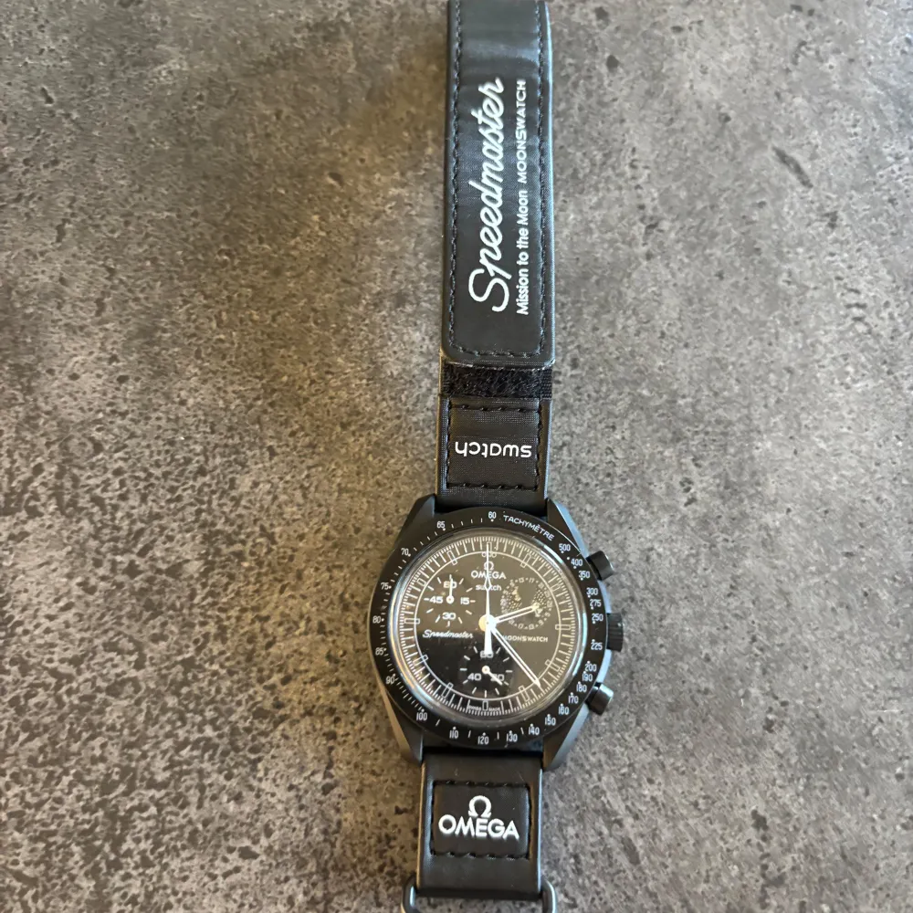 Säljer en stilren svart klocka från Omega x Swatch. Klockan har en klassisk design med vit text och detaljer på urtavlan. Armbandet är svart med Omega och Swatch-logotyper. Perfekt för den som gillar tidlös design. Fick denna i present så har inget kvitto och hittar tyvärr inte boxen därav priset. Asusteet.