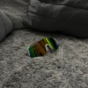 Sportiga solglasögon från TechFit Gear - Snygga och sportiga solglasögon med spegelglas i regnbågsfärger. Bågarna är vita med svarta detaljer och designade för en aktiv livsstil. Perfekta för utomhusaktiviteter och träning. Från TechFit Gear!