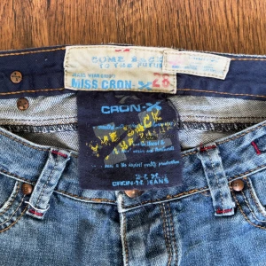 Blå jeans från Cron-x - Säljer ett par klassiska blå jeans från Cron-x. De har en låg midja och en straight passform. Jeansen är dekorerade med subtila slitningar på bakfickorna för en cool look. Lite uppklippta där nere för att få dom mer ”bootcut” liknande                     Ytterben - 102 cm Innerben - 82 cm Midja - 40 cm