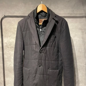 Morris kavaj jacka  - Snygg svart quiltad kavaj jacka från Morris med två knappar framtill och en diskret dragkedja. Kavajen har långa ärmar och en klassisk krage, perfekt för en stilren look. Storlek S men passar mer som M.