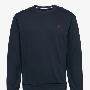 Mörkblå tröja från U.S. Polo Assn. - Säljer en stilren mörkblå tröja från U.S. Polo Assn. med ett rött broderat emblem på bröstet. Tröjan har långa ärmar och en rund halsringning med ribbade kanter. Perfekt för en avslappnad look. Jag har använt den typ bara 3 gånger max