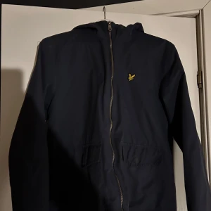 Lyle and scott vår/höst jacka  - Säljer en stilren svart vindjacka från Lyle & Scott med dragkedja och huva. Använd en del men fortfarande snygg och hel. Skick 7/10. Pris kan diskuteras vid snabb affär 