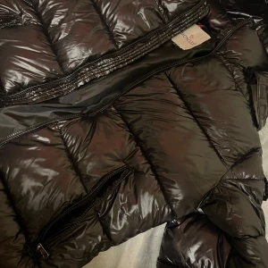 Svart dunjacka från Moncler - Säljer en snygg svart dunjacka från Moncler. Jackan har en glansig finish och är utrustad med dragkedja. Perfekt för kyliga dagar när du vill hålla stilen. Helt ny aldrig använd, fel storlek för mig! Pris kan diskuteras! Skriv om ni har frågor!
