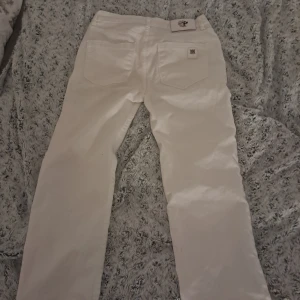 Vita byxor från Philipp Plein - Snygga vita byxor från Philipp Plein med coola detaljer som en dödskalle och stjärna på logotypen. Byxorna har en rak passform och är perfekta för en stilren look. De har fickor både fram och bak samt en knapp och dragkedja i gylfen.