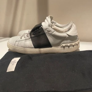 Valentino sneakers i vitt och svart - Snygga Valentino sneakers i vitt med en bred svart rem över ovansidan. Skorna har en klassisk design med rund tå och en bekväm sula. Perfekta för en stilren look. Skriv för mer bilder🤝🏼