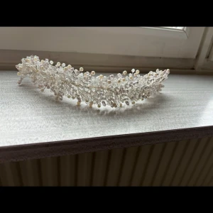 Elegant hårsmycke med pärlor och kristaller - Vackert hårsmycke dekorerat med vita pärlor och glittrande kristaller. Perfekt för speciella tillfällen som bröllop eller bal. Smycket har en böjbar design som gör det enkelt att anpassa efter frisyr.